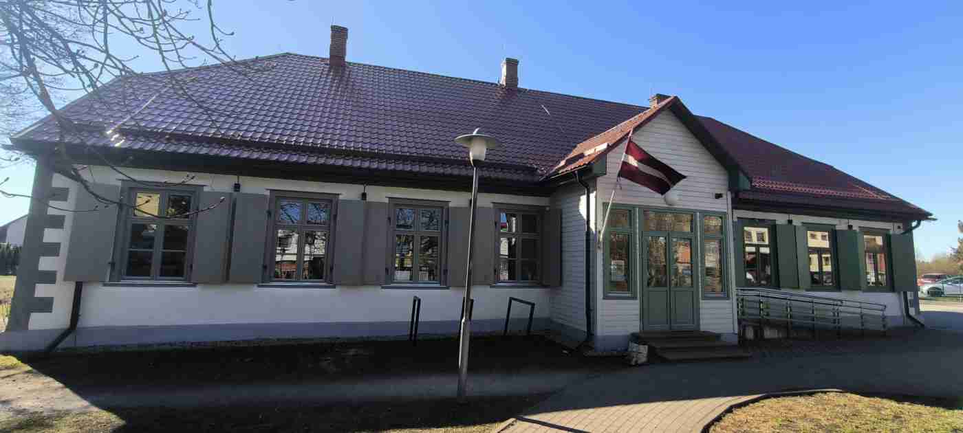 Vienstāvu ēka, Latvijas karogs pie ieejas, ir uzbrauktuve, mājas priekšā bruģēts celiņš