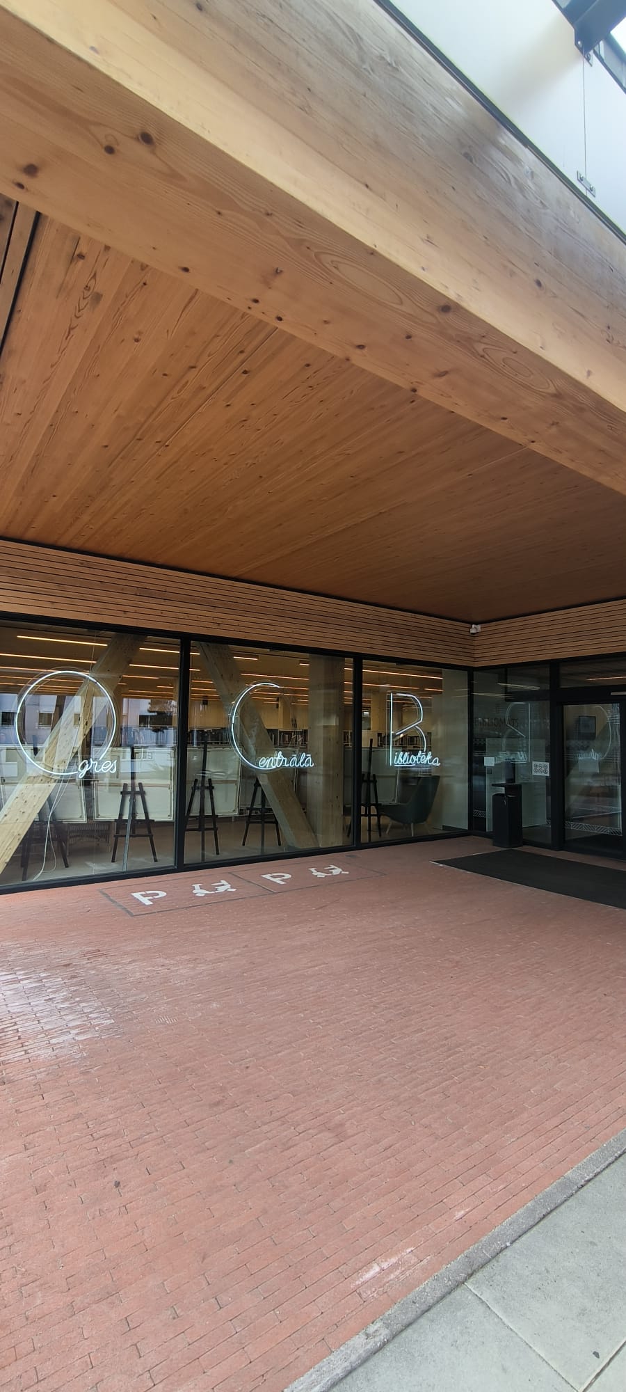 Pie bibliotēkas ieejas, uz zemes apzīmējumi, logos burti OCB