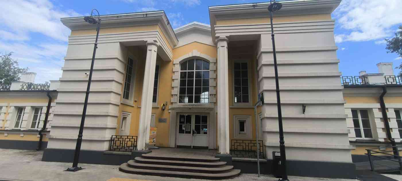 Dzelzceļa stacijas ēka dzeltenā, baltā krāsē. Pirms ieejas durvīm kāpnes
