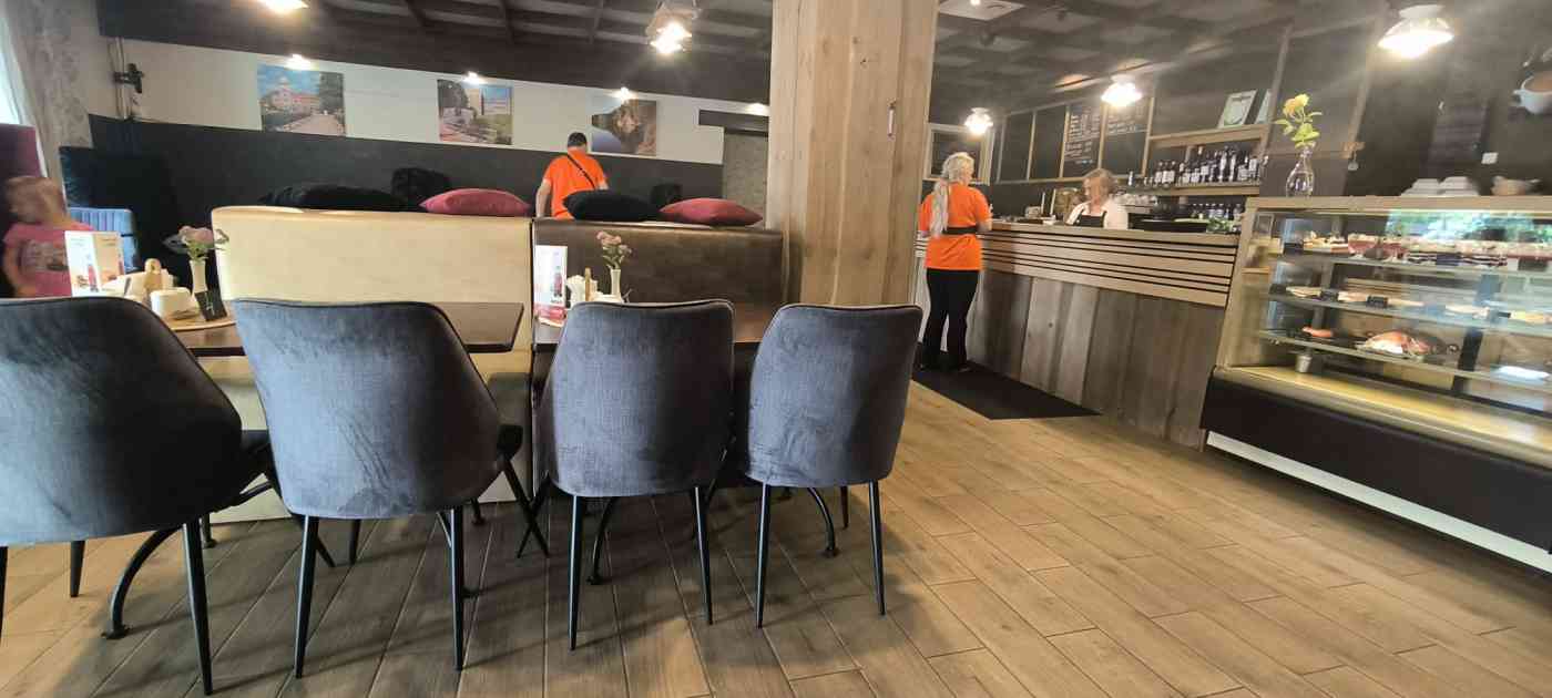 Krodziņa iekšpusē 4 cilvēki, vairāki galdi, krēsli, augsta lete, pie sienām fotogrāfijas