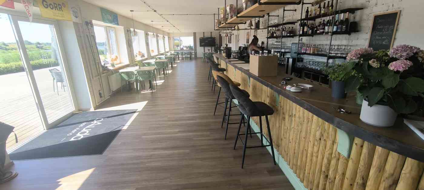 Iekštelpa. Pie ieejas durvīm paklājs. Lete, daudz galdu, krēsli. Uz letes puķpods