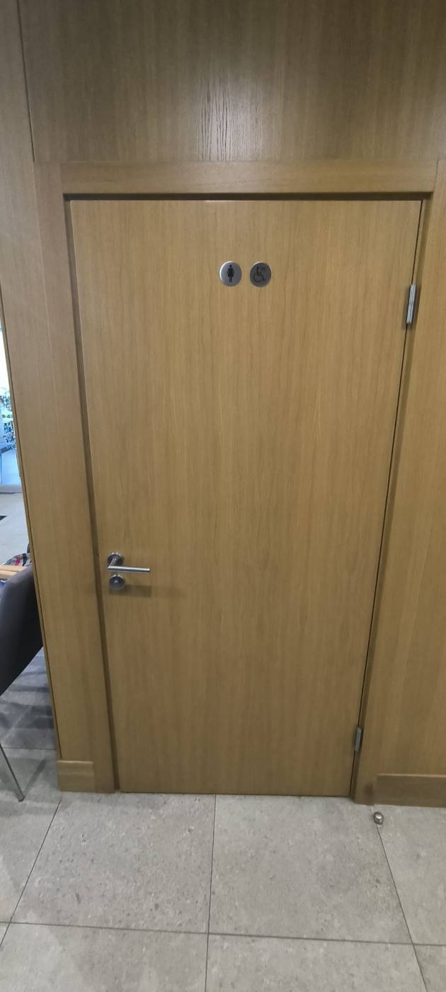 Tualetes durvis brūnā krāsā. Uz durvīm sieviešu un cilvēku ratiņkrēslā simbols