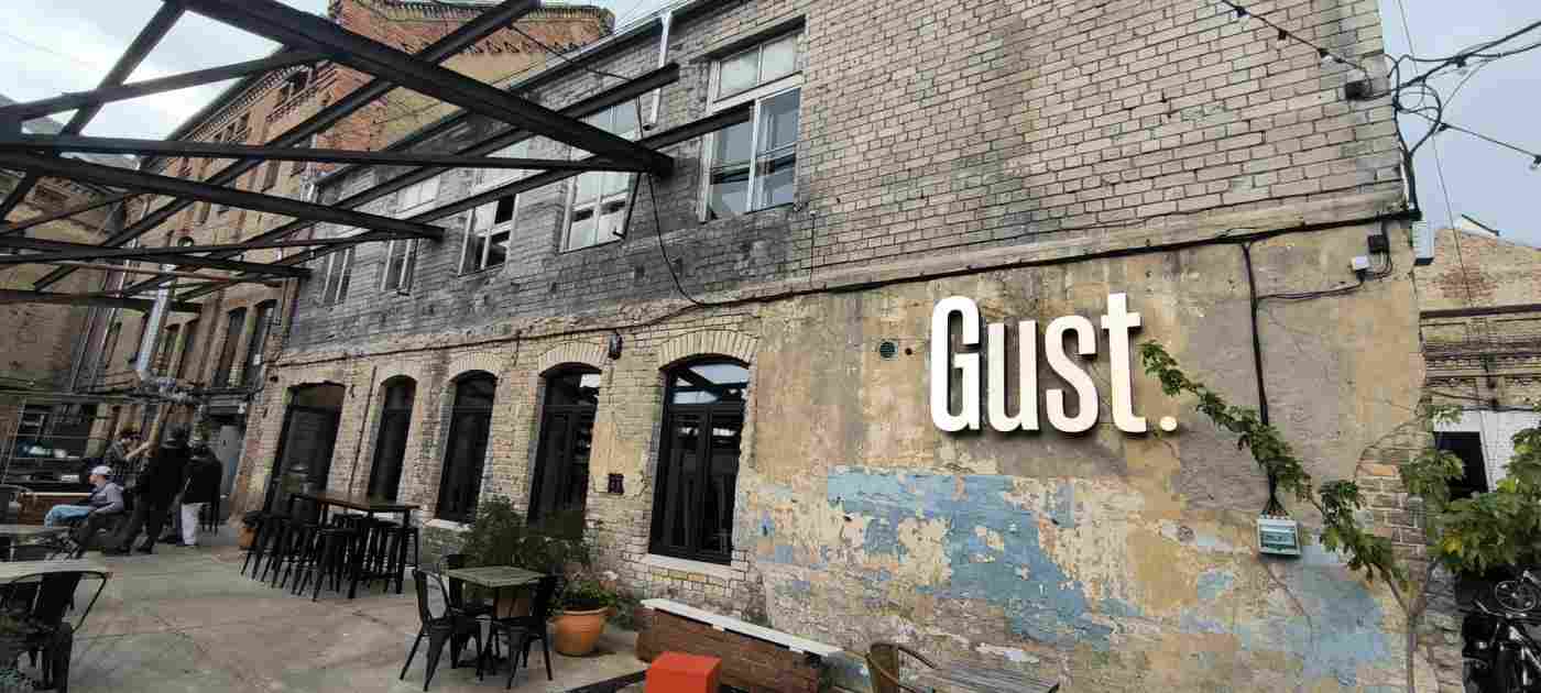 Divstāvu ķieģeļu ēka. Mājas priekšā galdi, krēsli, puķpodi